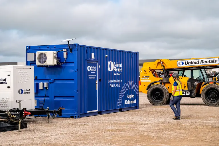 Un employé de United Rentals se dirigeant vers un conteneur bleu de fournitures à la demande sur un chantier
