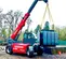 Side view of red Magni telehandler with extended boom and enclosed cabin lifting a power transformer outdoors on a worksite.