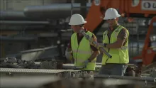 Two men on a construction site wearing hard hats, safety vests and safety glasses.