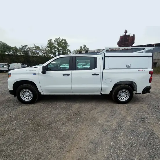 Side view of a white Chevrolet Silverado crew cab pickup truck with a white utility bed cap