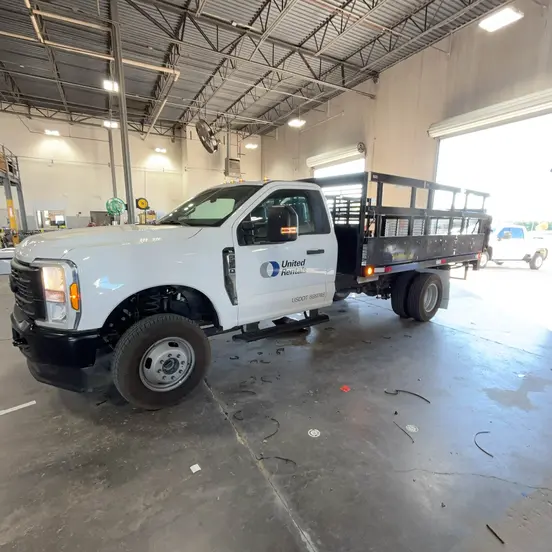 View from left side a white flatbed truck is parked in a large garage or service hall.